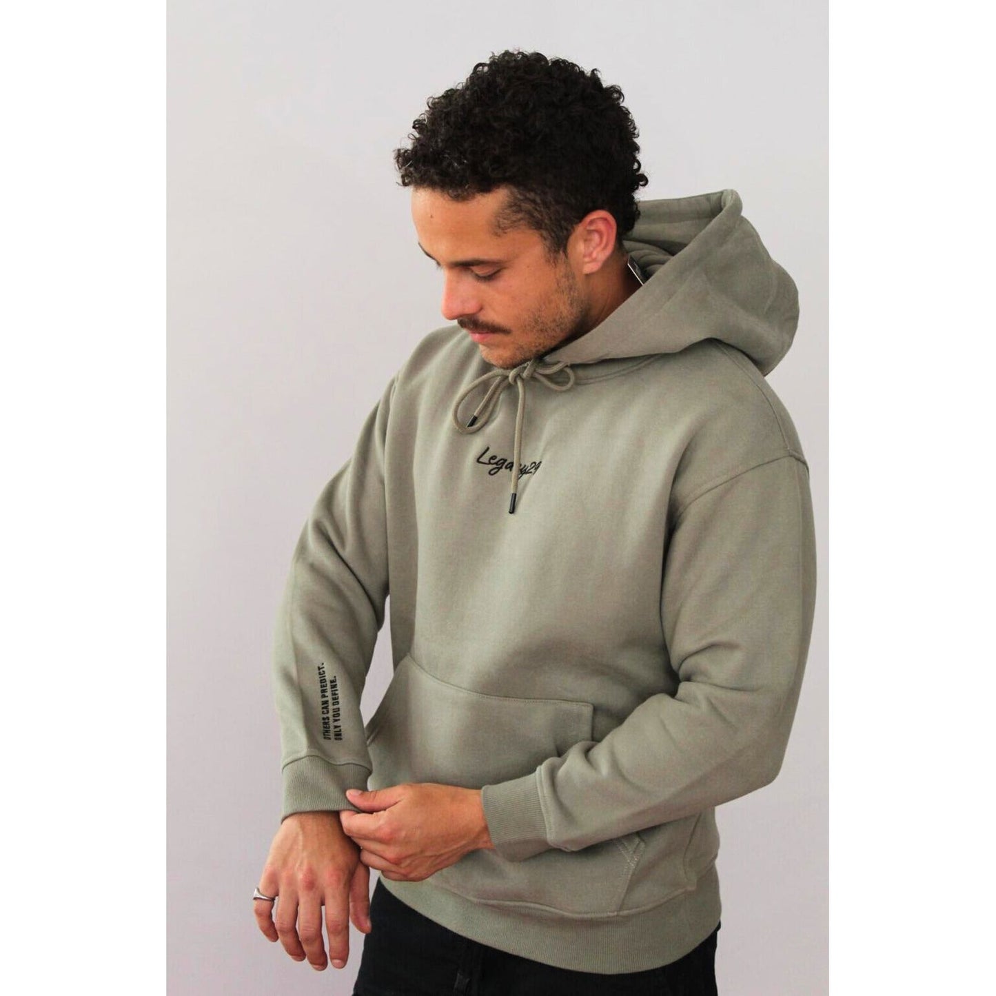 Man in Legacy29 Grateful Green hoodie looking at sleeve text detail. Premium oversized hoodie designed for comfort and resilience.