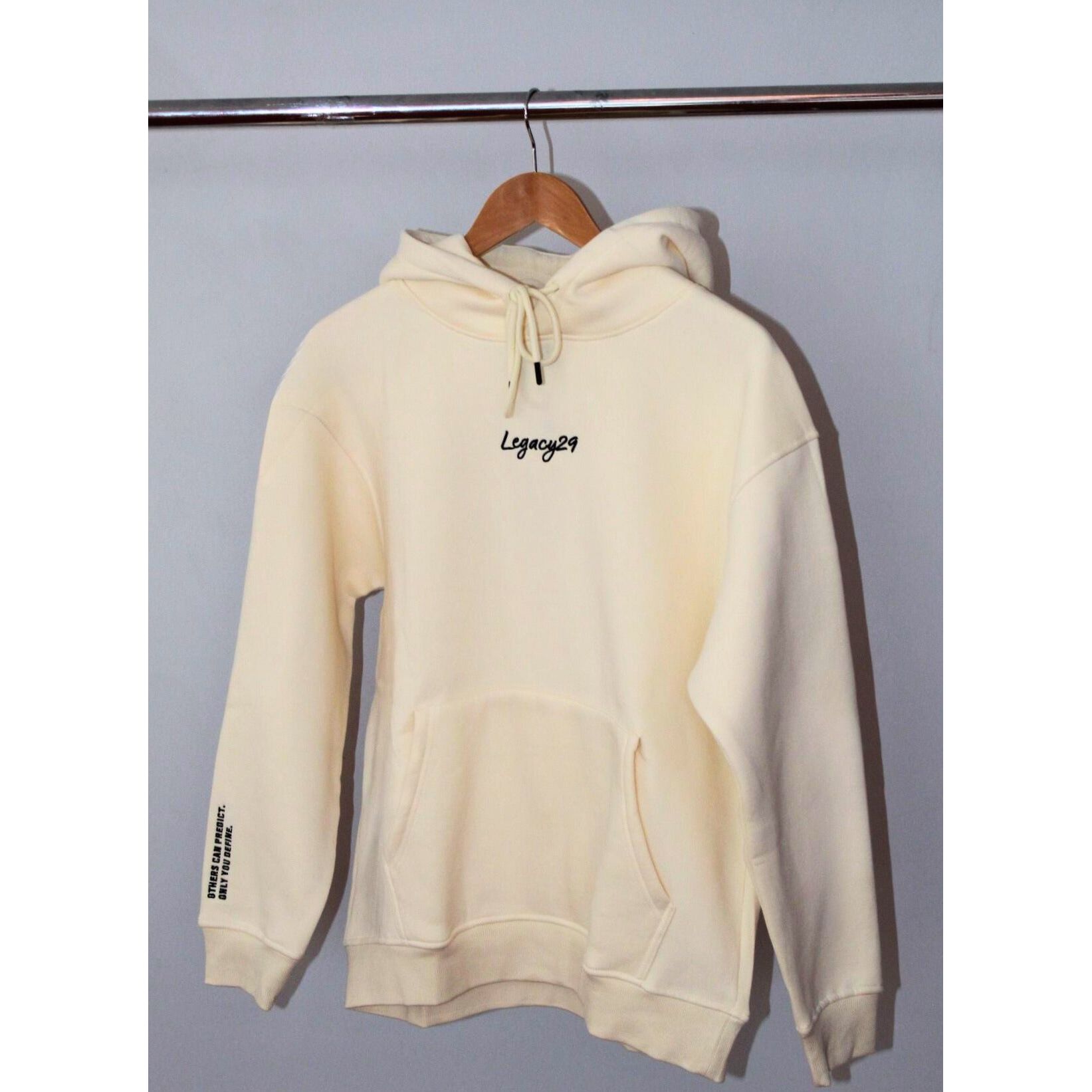 Legacy29 Cloud 9 cream hoodie hanging on a wooden hanger. Soft oversized design with embroidered logo on the chest, offering comfort and resilience.