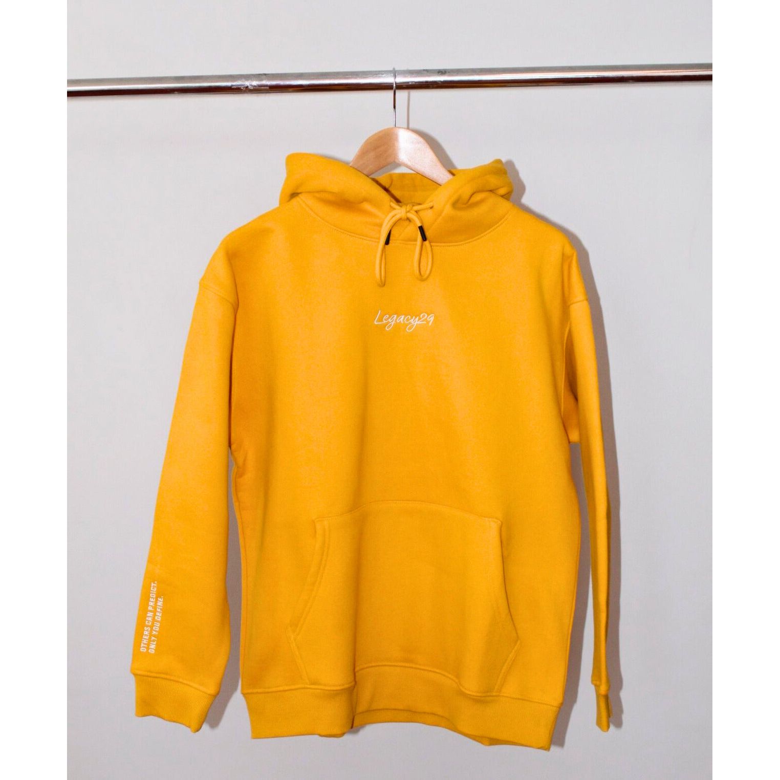 Legacy29 Golden Glow Yellow hoodie hanging on a wooden hanger. Soft, oversized fit with front pocket and embroidered logo for a stylish, cozy look.