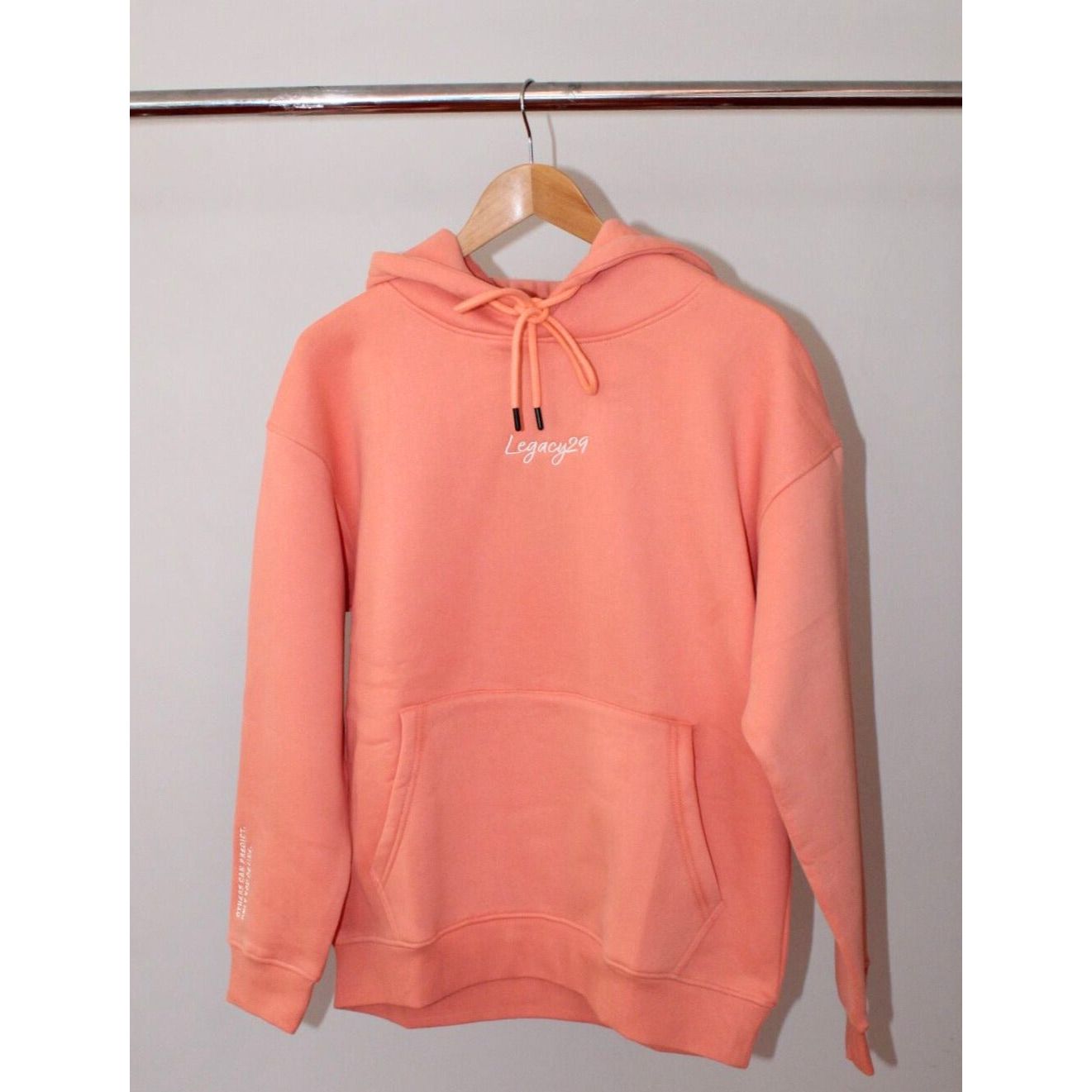 Legacy29 Resilience Collection: Confident Coral Hoodie displayed on a wooden hanger, showcasing its oversized fit and kangaroo pocket.