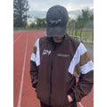 Person wearing a brown jacket with white accents and a black cap on a track field.
