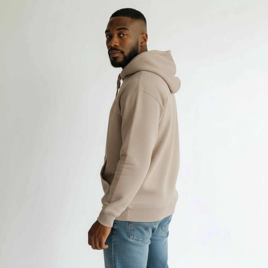 Man wearing a beige hoodie and blue jeans against a white background