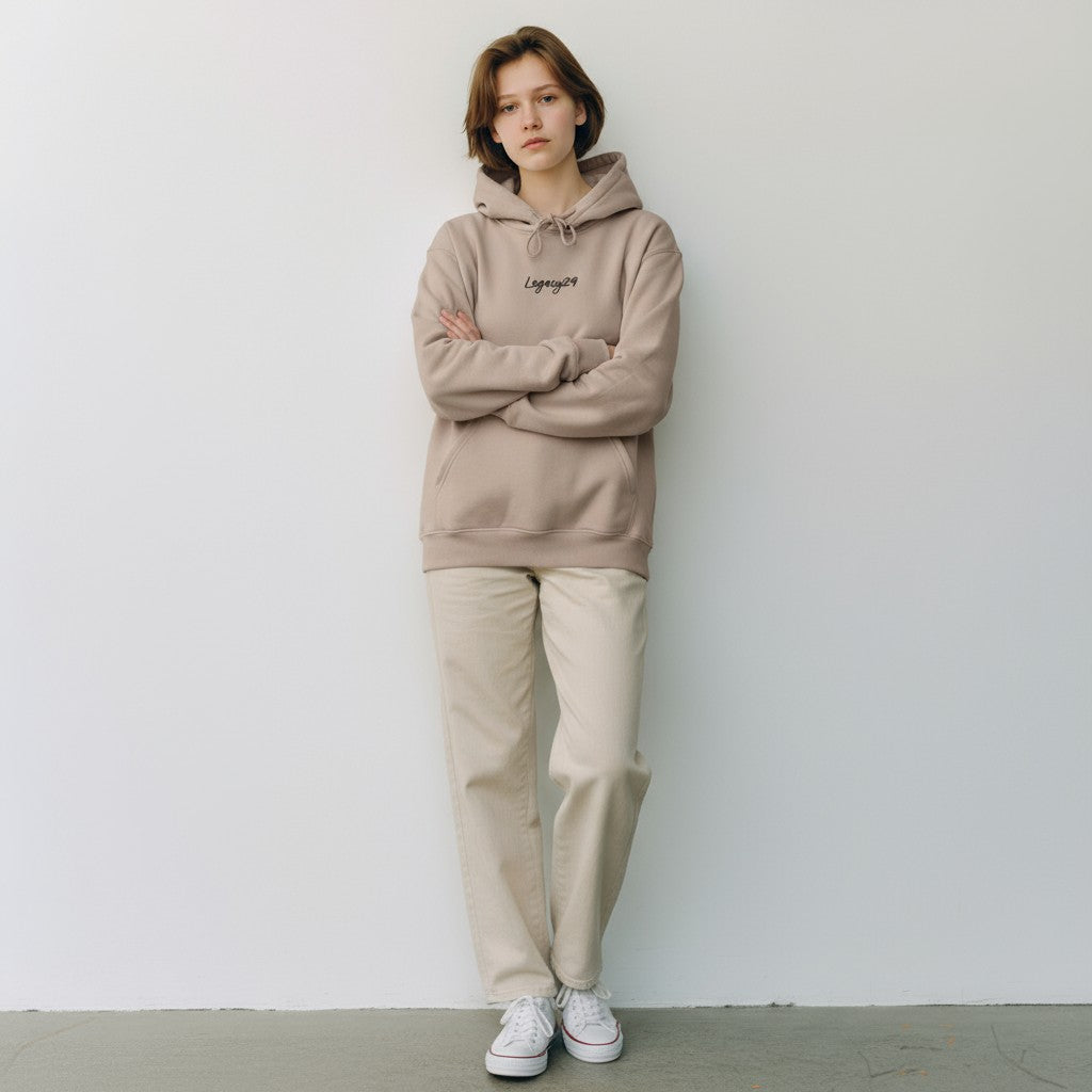Person wearing a beige hoodie and pants standing against a white wall.