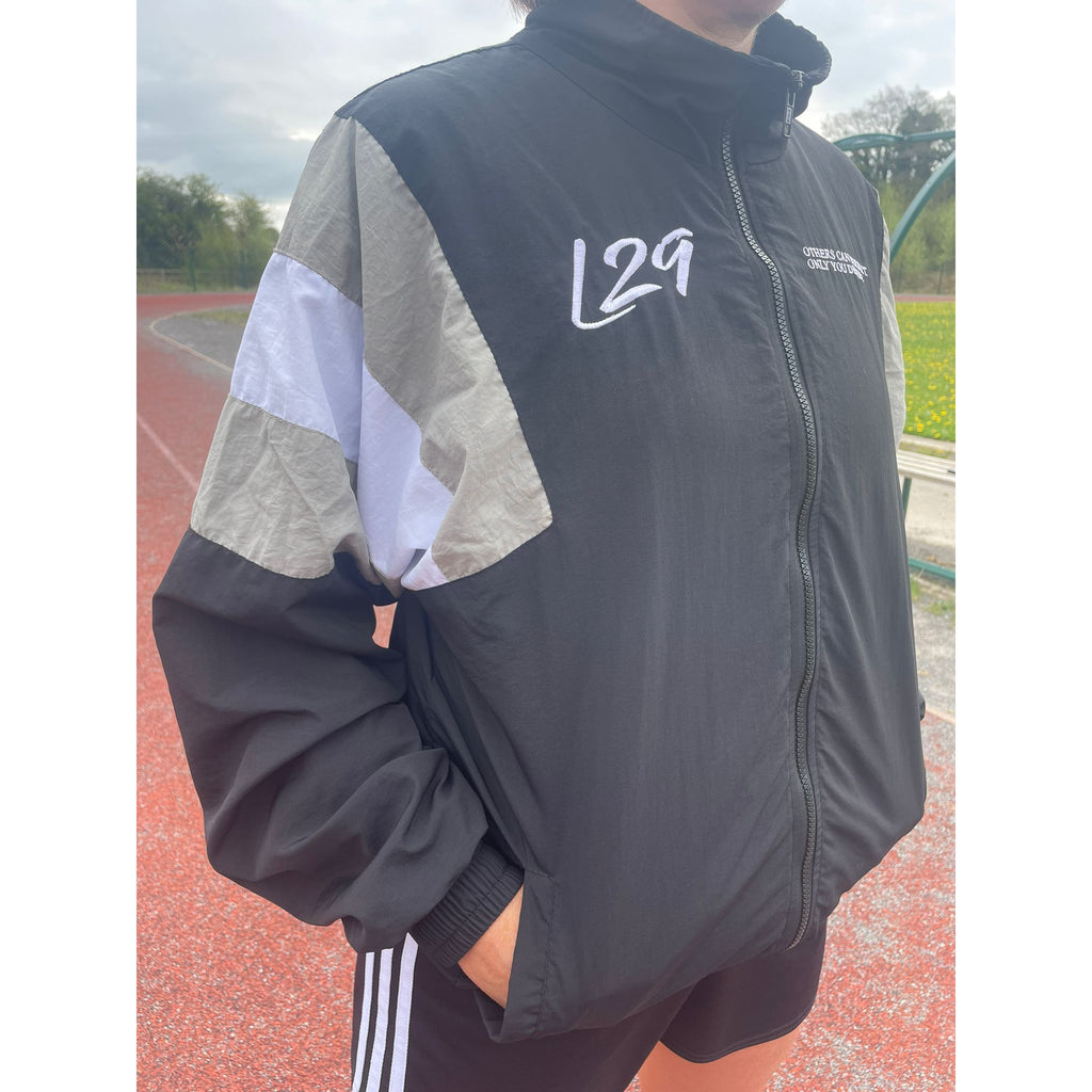 Person wearing a black jacket with a logo on a track field