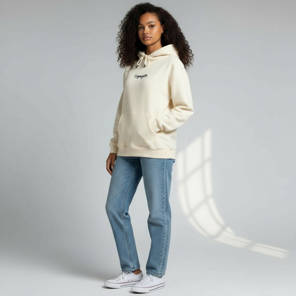 Woman wearing a cream hoodie and blue jeans on a gray background