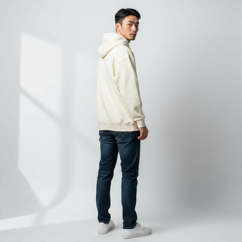 Man wearing a cream hoodie and dark jeans on a white background