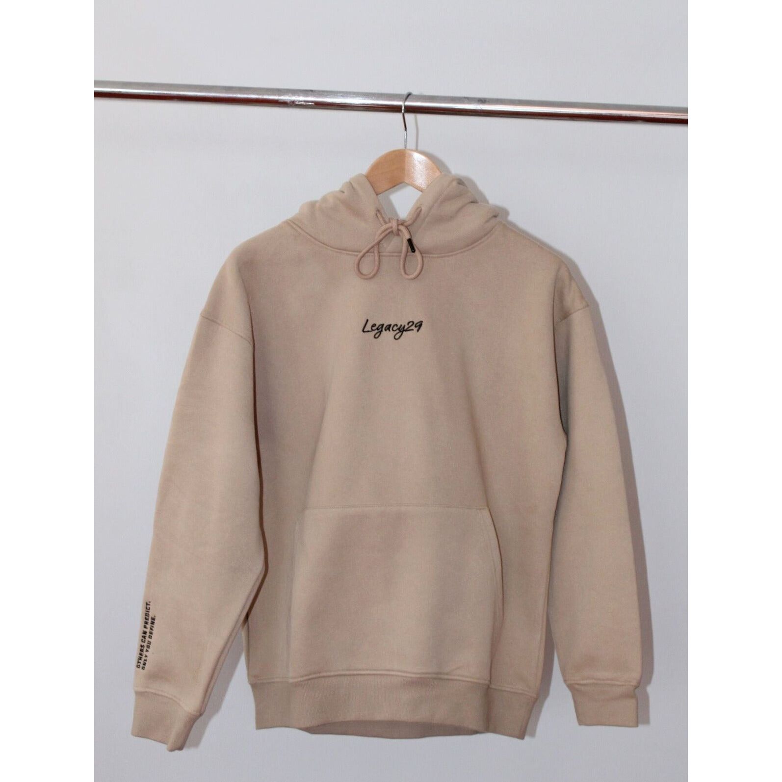 Legacy29 Desert Dawn Beige hoodie hanging on a wooden hanger, showcasing its minimalist design and premium fleece-lined cotton fabric.