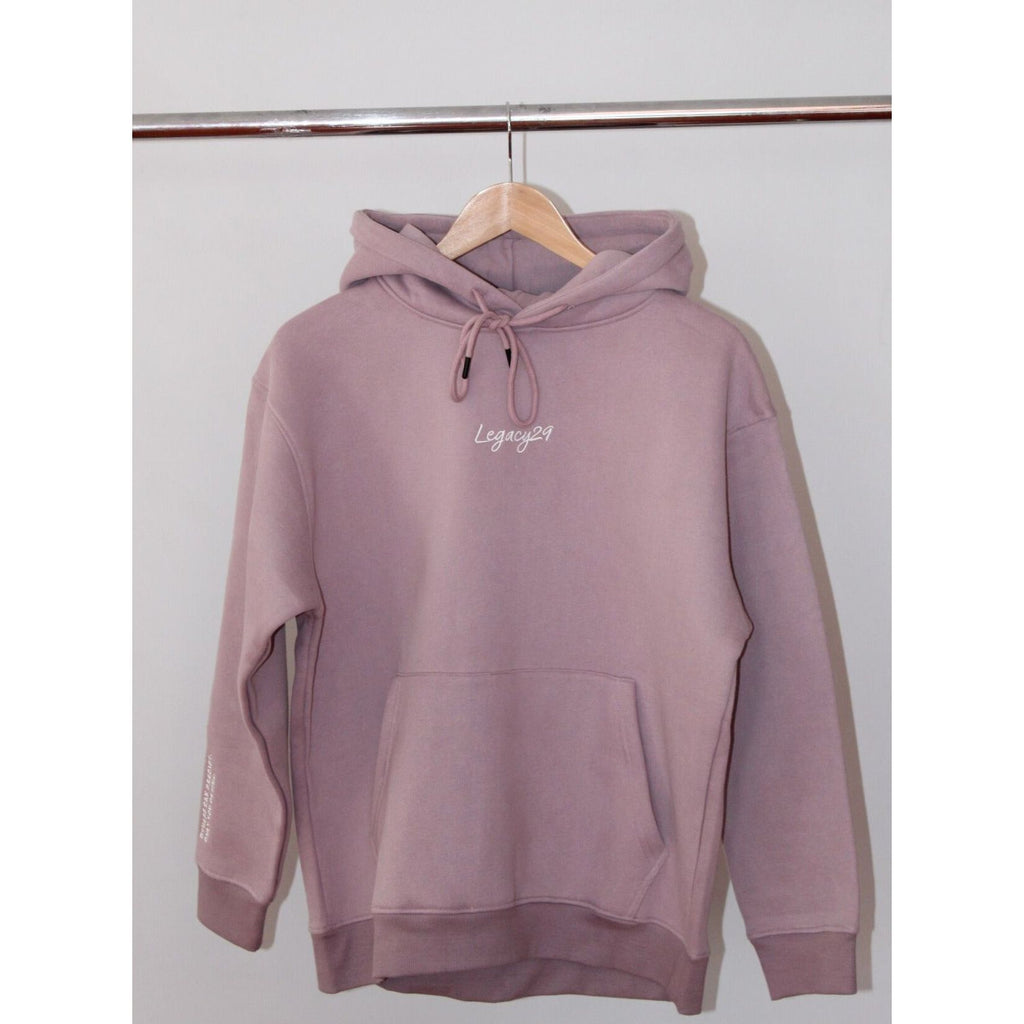 Legacy29 Lavender and Let Go comfort hoodie hanging on a wooden hanger. Soft lavender shade with embroidered logo, designed for resilience and relaxation.