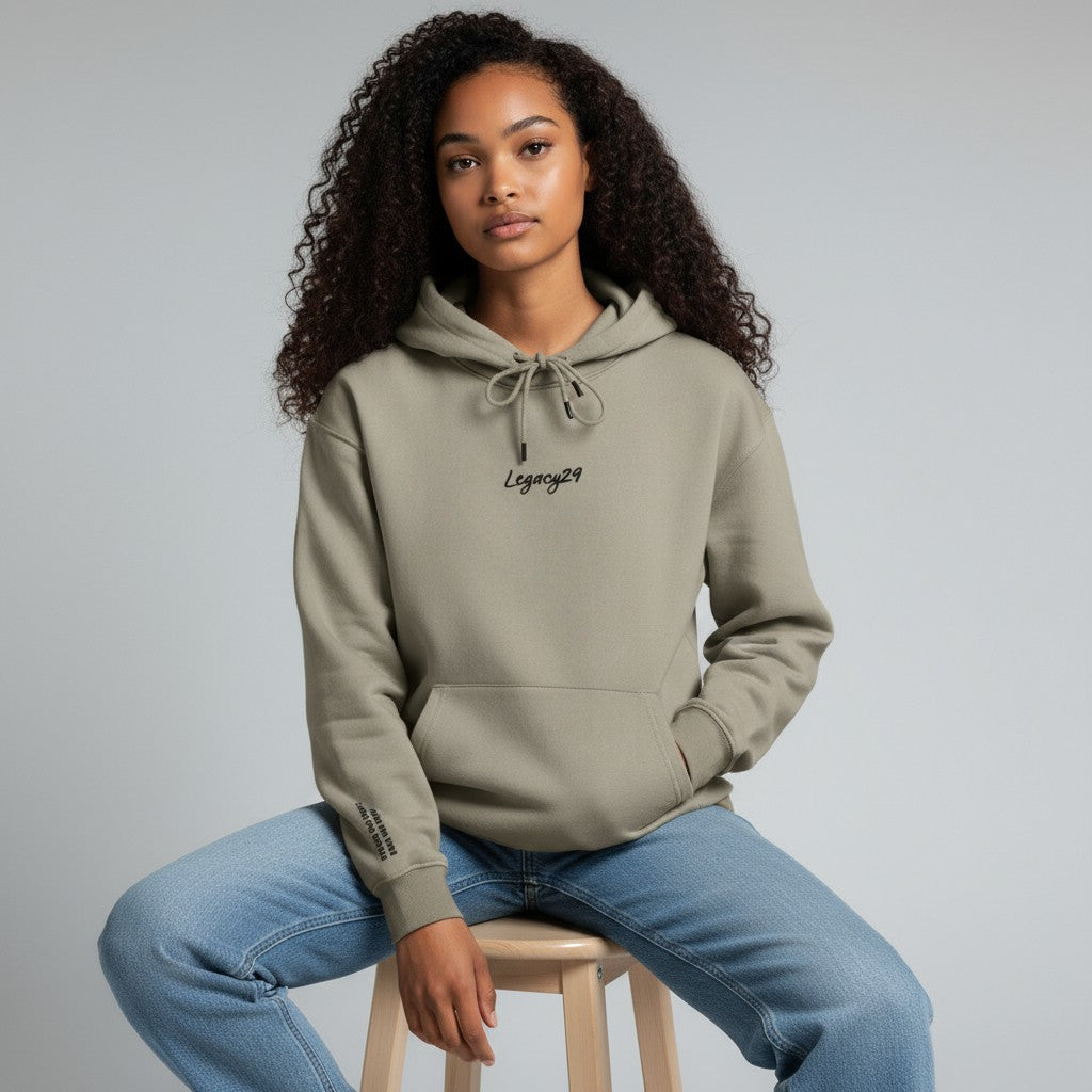 Woman wearing a gray hoodie with 'Legacy29' logo, sitting on a stool against a gray background
