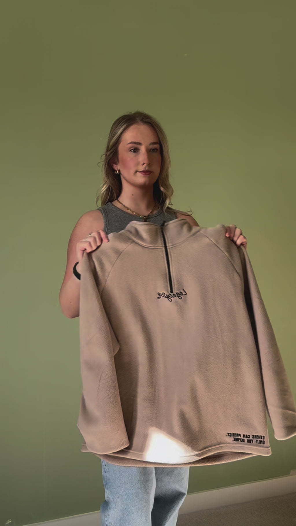 Woman holding up the Ecru Sandstone Fearless Fleece by Legacy29, showcasing its oversized fit, soft fabric, and inspiring mental health message.