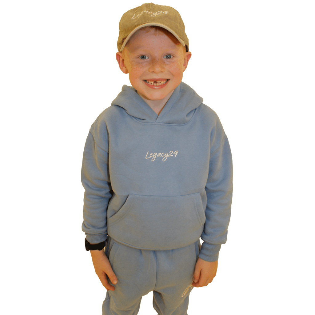 Smiling child wearing the Legacy29 Junior Blue Comfort Set, including a cosy hoodie and matching tracksuit bottoms. Perfect for everyday wear.