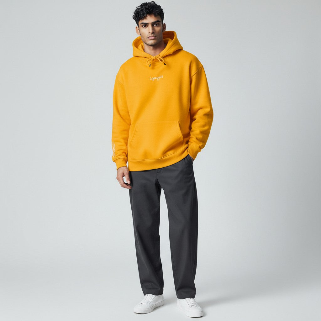 Man wearing a bright yellow hoodie with a brand logo on a light gray background